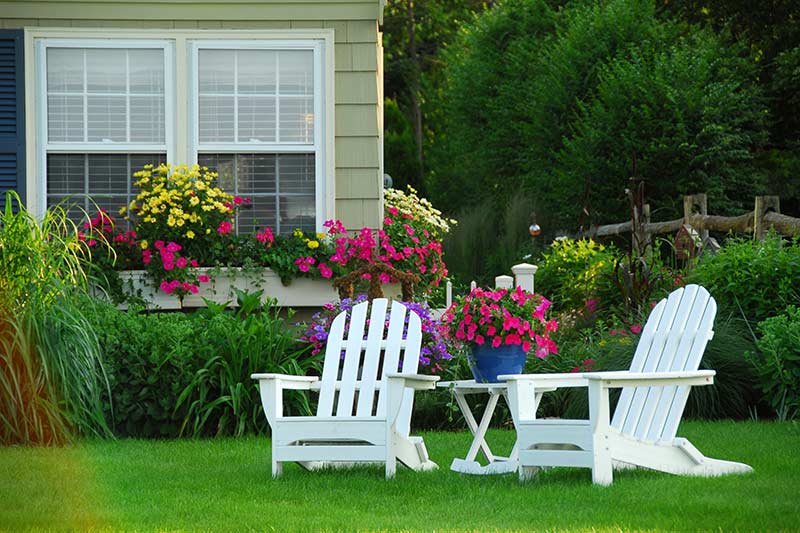 2 white adirondack chairs near colorful flower beds